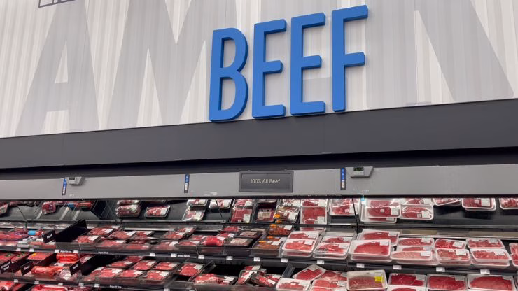Walmart beef section with a large overhead sign labeled ‘BEEF’ and packaged beef products displayed in coolers below.
