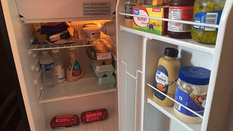 Inside view of a hotel room mini fridge stocked with carnivore diet essentials like raw meat, eggs, and butter.