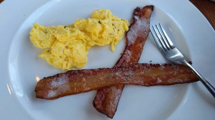 Small serving of eggs and bacon on a restaurant plate, representing a simple carnivore-friendly meal while dining out with friends.