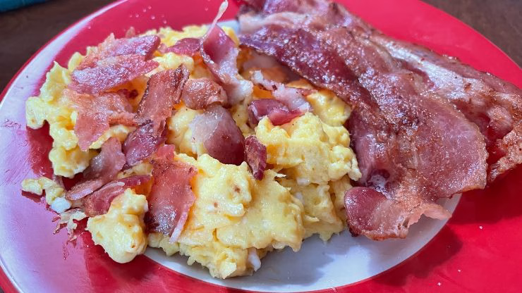 Plate of scrambled eggs topped with chopped bacon and served with bacon on the side